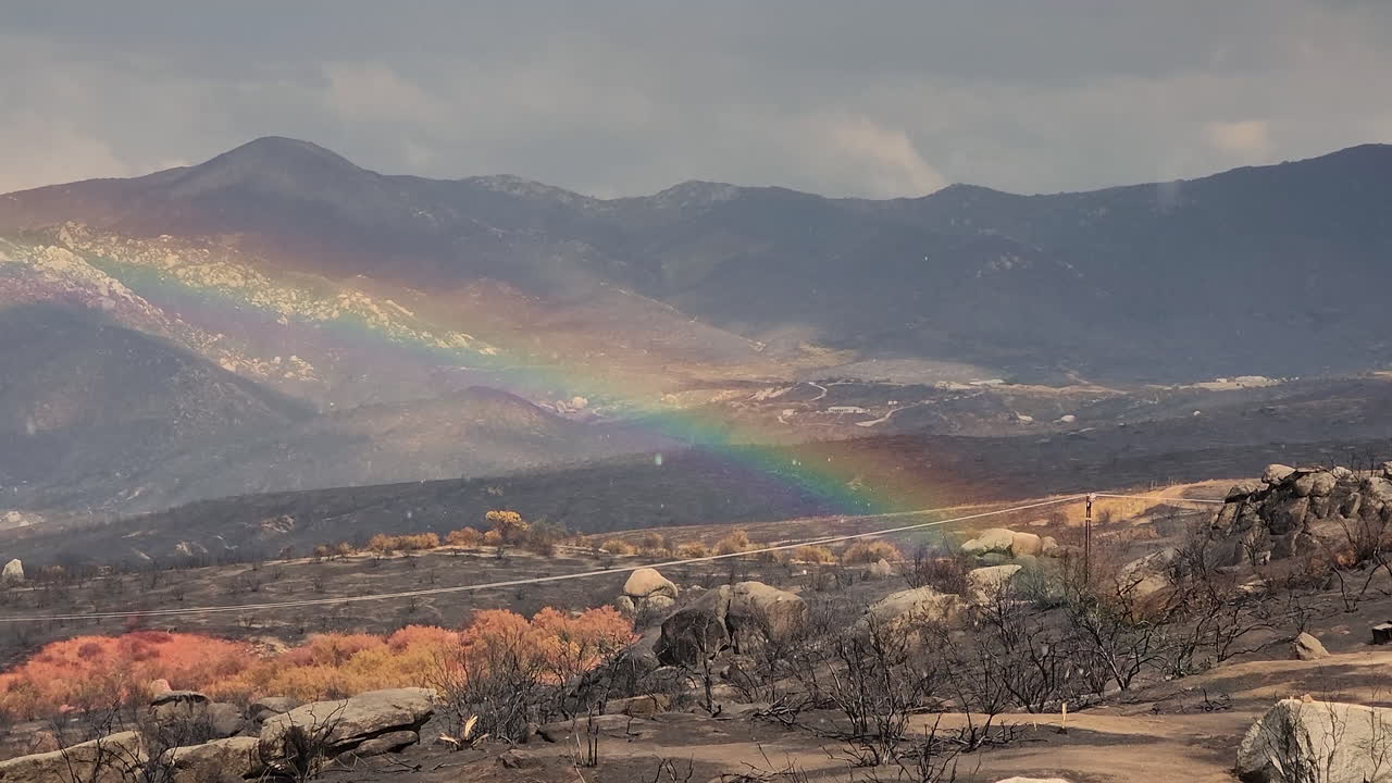 gotas de lluvia cayendo sobre un lugar desolado quemado con un gran arco iris colorido frente a las montañas en el fondo