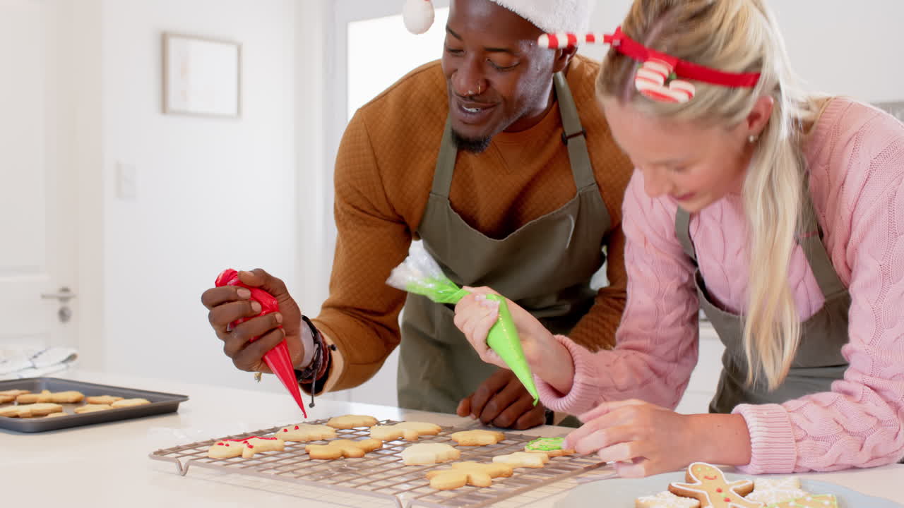 Coppia multietnica che decora biscotti di Natale, godendosi la preparazione festiva a casa.