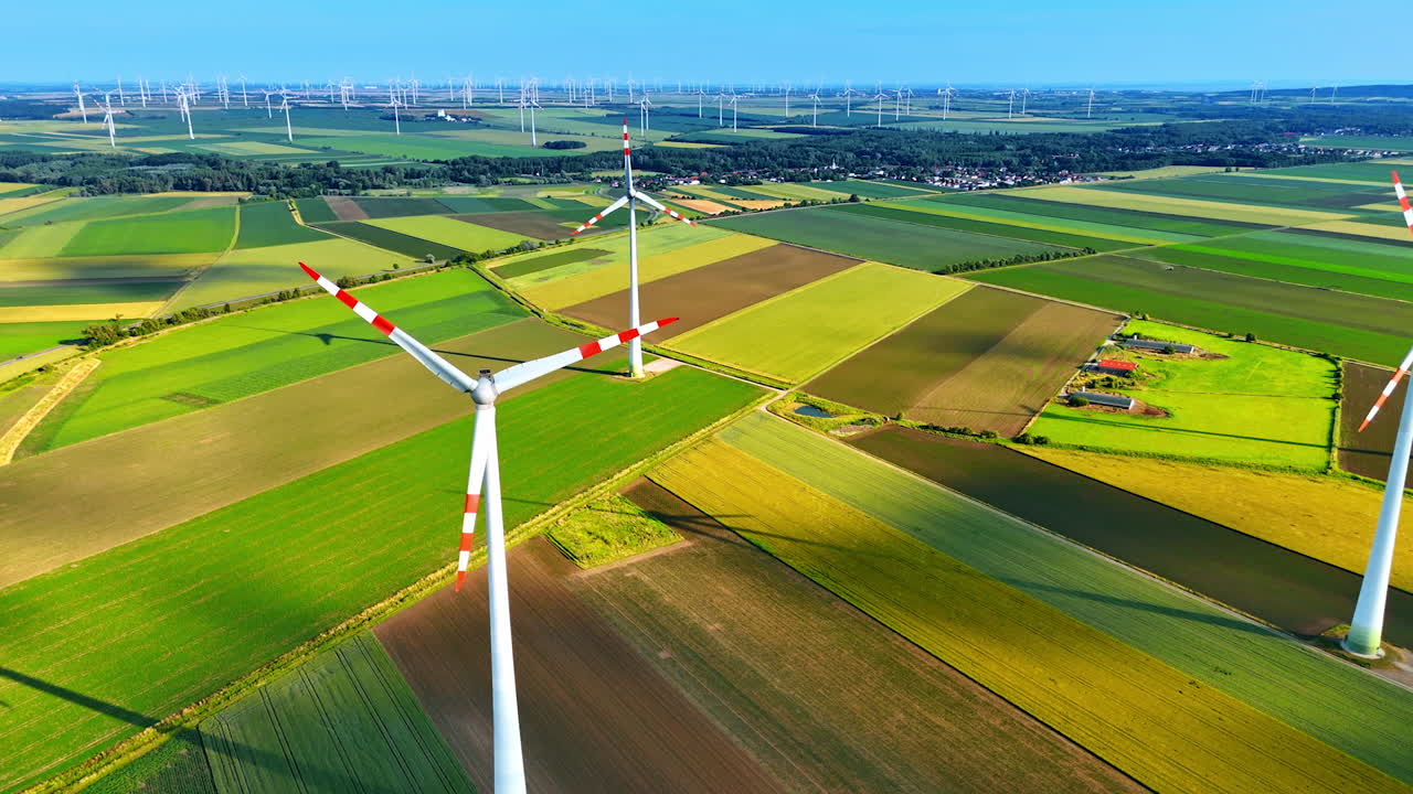 Turbines produce energy in fields. Wind turbines stand tall in lush green fields, generating renewable energy under a clear blue sky during daylight