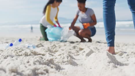 Diverse-group-of-female-friends-putting-rubbish-in-refuse-sacks-at-the-beach