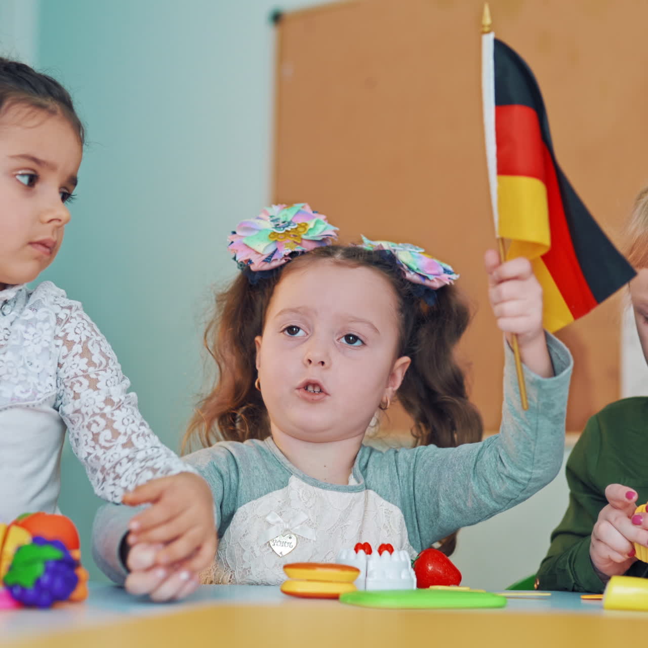 Girls sitting with small flags at primary school. One little girl tries to take German flag from other student on the classroom background.
