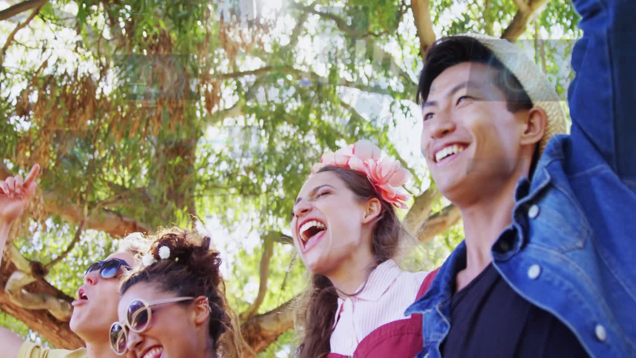 Group of four cheering beneath tree, camera tilting back, HUD panels overlaying faces for marketing