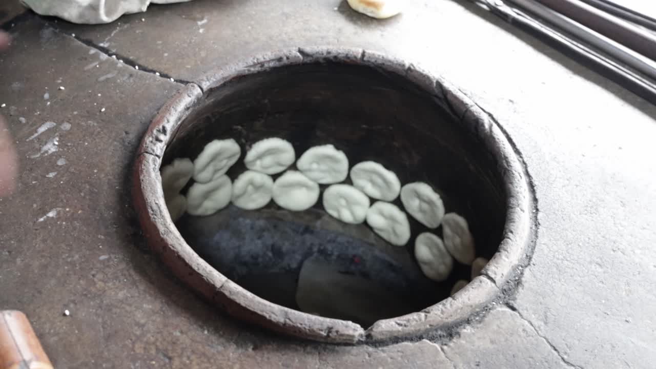 Food vendor putting flat dough in clay oven to make grilled Chinese flat bread or "Huping" in traditional way