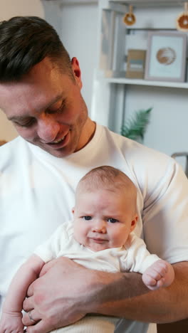 caucasian man wearing white t-shirt holding a tiny newborn in white t-shirt. like father like son. close up. vertical video