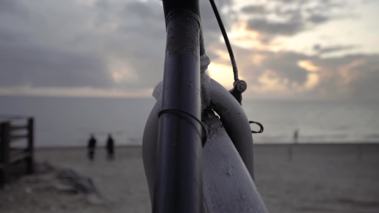 Vintage '80s touring bicycle by the sea with a man running along the shore and people walking down the beach at sunset SLOW MOTION 120 FPS