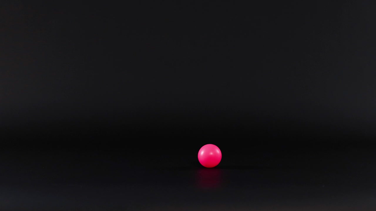 A pink ball rolls across a dark surface