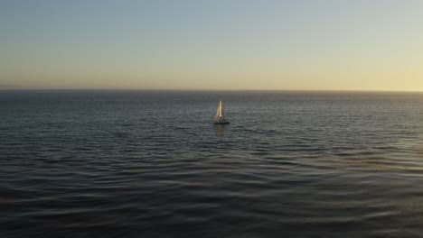 drone flies above sailboat alone at sea, birds eye sunset view