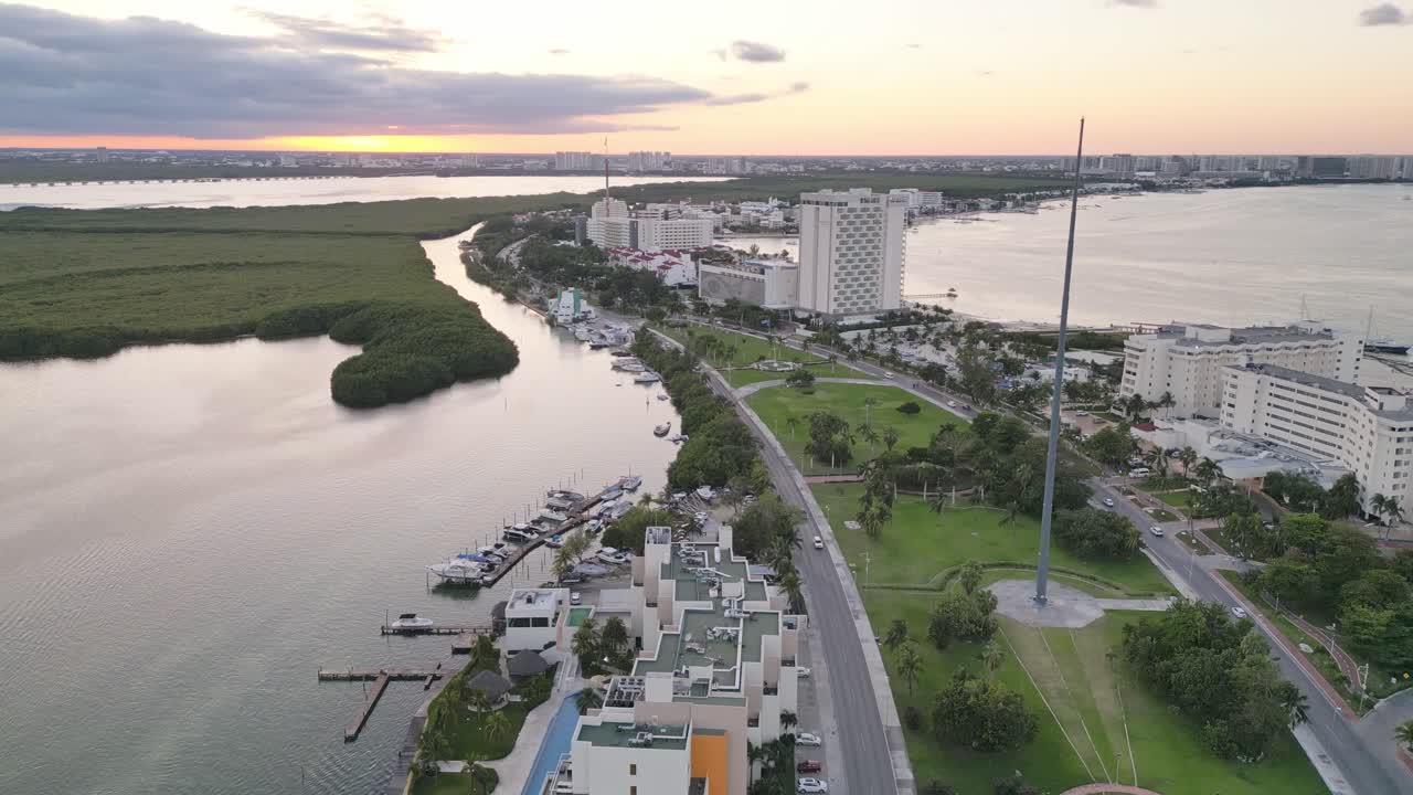Cancun at sunset with a waterfront, lush greenery, and modern buildings, aerial view