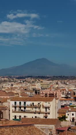 vertical aerial view to mount etna from catania's urban area in a sunny day. panoramic drone shot above rooftops in the city of catania in sicily. europe's active volcano.