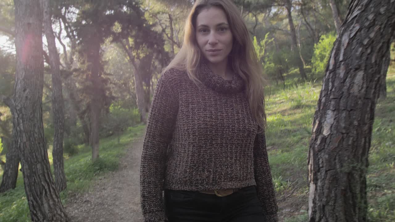Young woman smiles at camera while walking at a path among pine trees on Lycabettus hill, gimbal