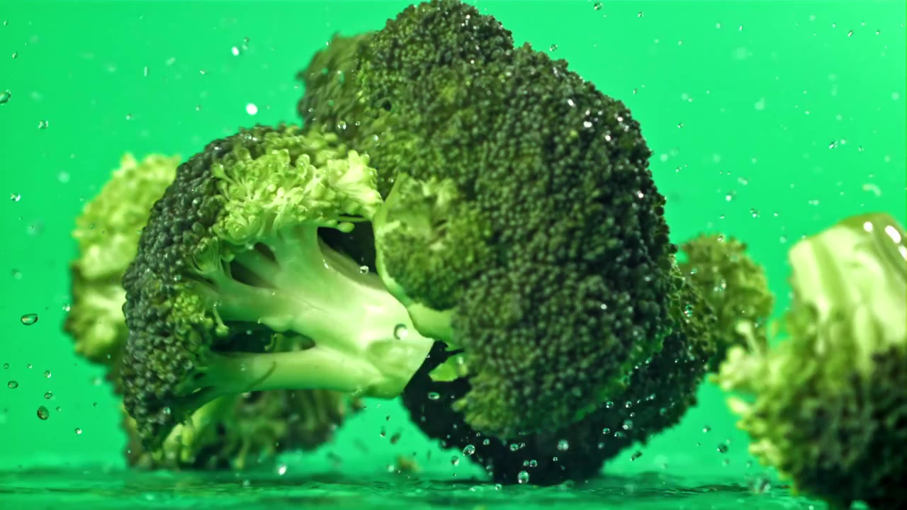Fresh Broccoli Florets Falling into Water and Splashing on Green Screen