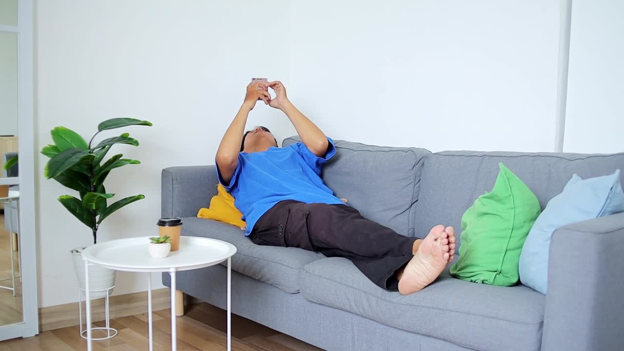 Relaxed man scrolling phone on comfortable sofa enjoying casual moment at home