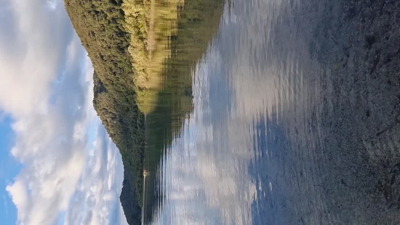 Vertical view of blue lake at the lakeside showing the reflection of the fern covered mountains and hills in Rotorua New Zealand