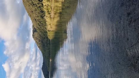 vista vertical del lago azul a la orilla del lago que muestra el reflejo de las montañas y colinas cubiertas de helechos en rotorua, nueva zelanda