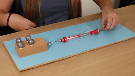a person uses a spring scale to measure force needed to slide weights on cardboard, illustrating friction principles