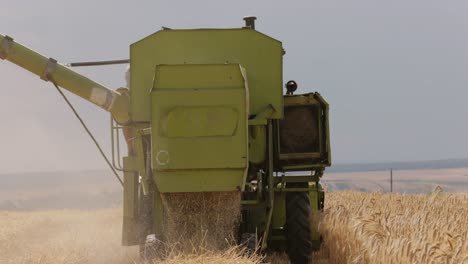 Cerrar-La-Vista-En-Cámara-Lenta-De-La-Parte-Trasera-De-Una-Vieja-Cosechadora-Verde-En-El-Trabajo-Descargando-Paja-Detrás-De-Ella