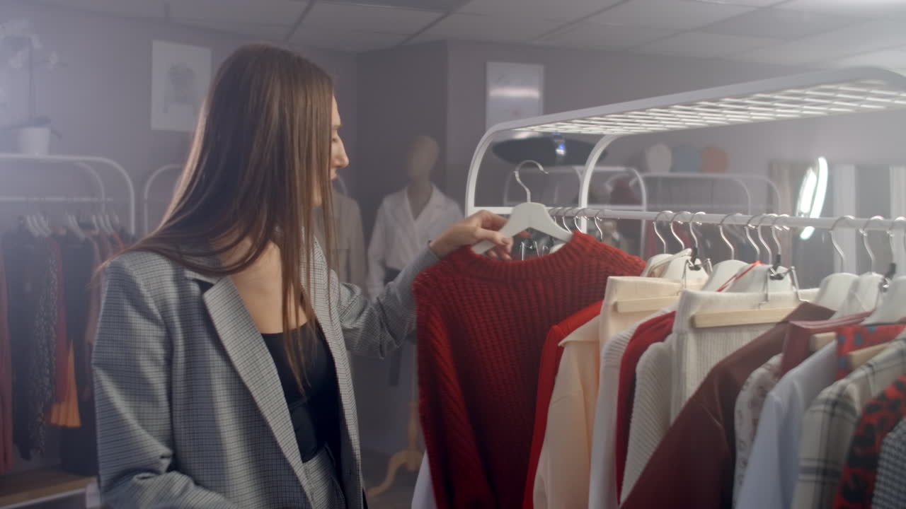 una joven morena en una tienda de ropa elige un vestido para colgar en un colgante y lo prueba. compra un vestido en la tienda. busca y elige ropa en una boutique. toma el vestido del colgante en el soporte