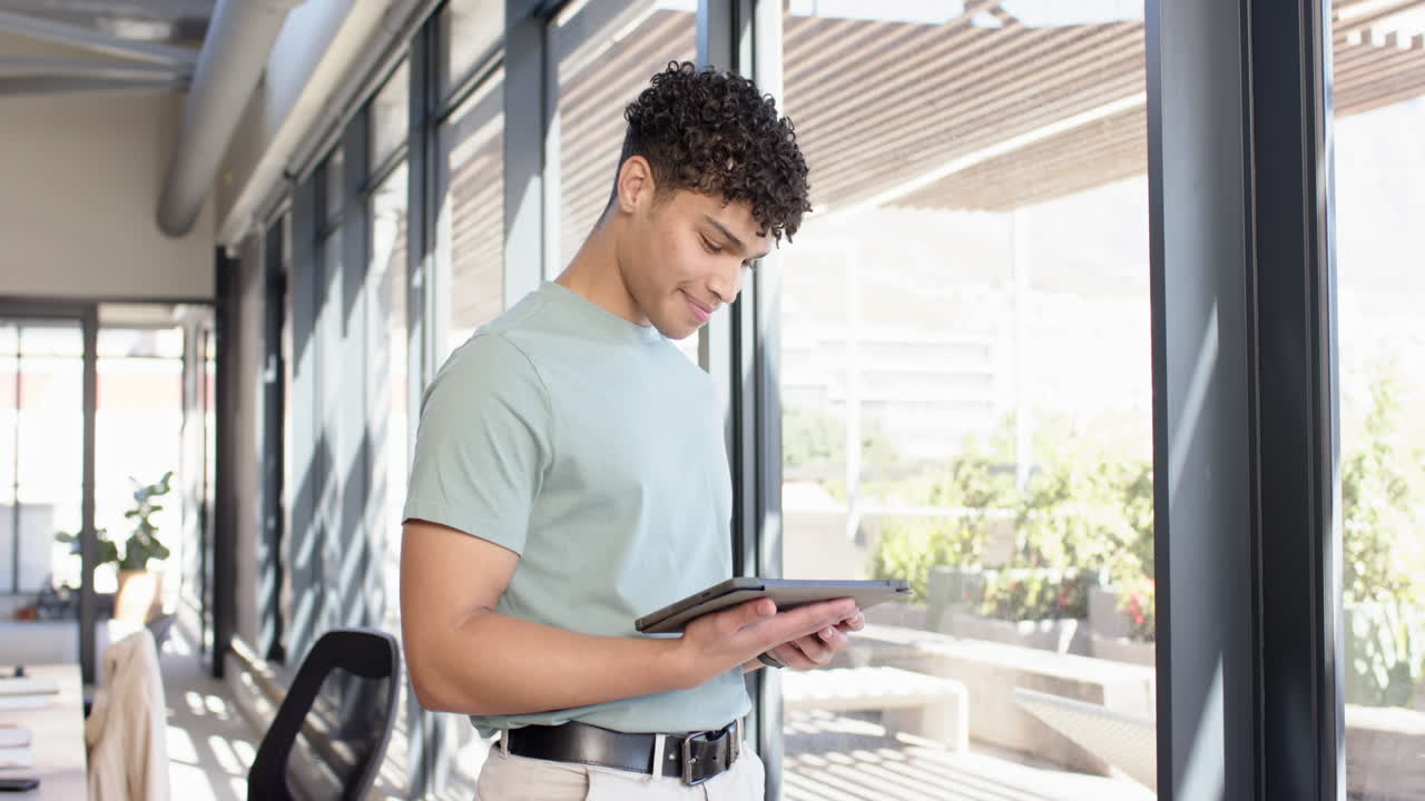 Using tablet, young man standing in modern office, checking design plans, copy space