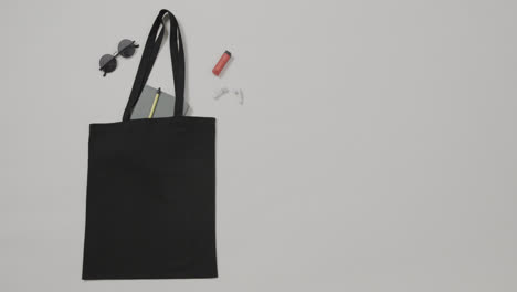 black bag with sunglasses, notebook, lipstick on white background, copy space, slow motion