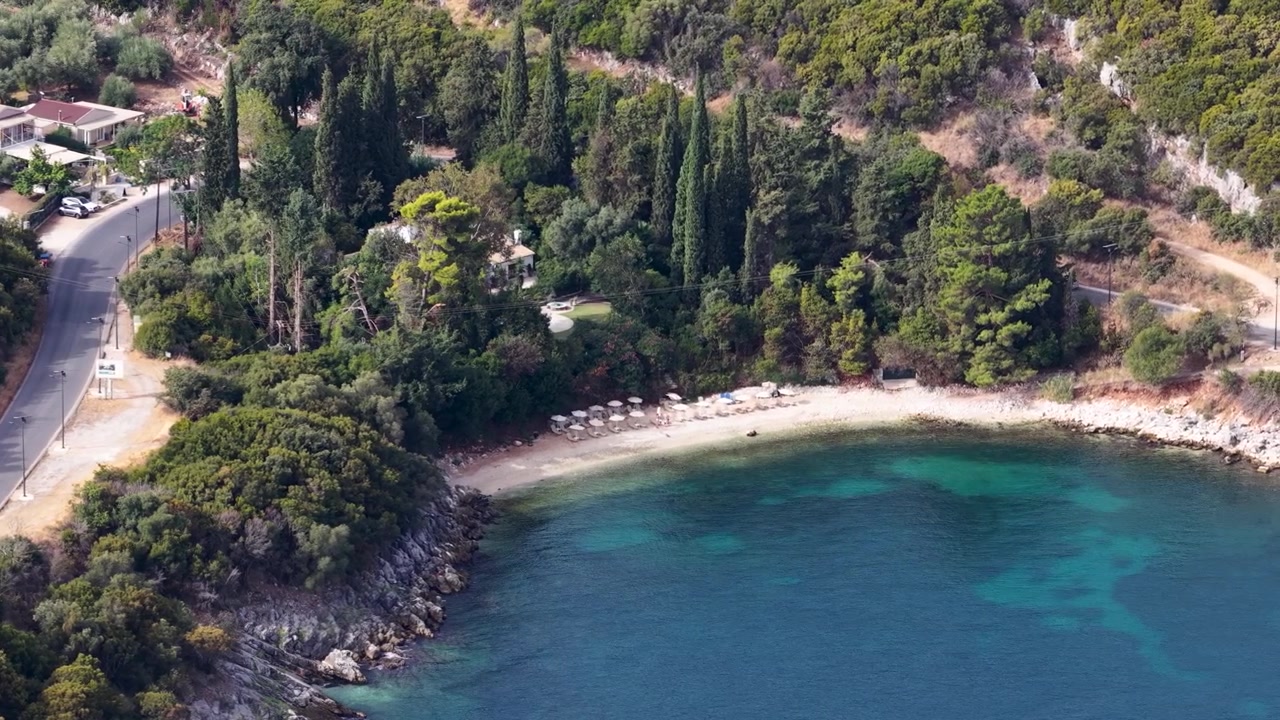 Aerial Drone View of Beautiful Tropical Turquoise Beach Cove with Cypress Trees and Coastal Road in Kassiopi, Corfu Island, Greece