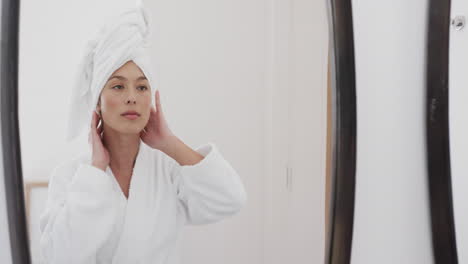 Happy-biracial-woman-touching-her-face-looking-in-mirror-in-bathroom,-slow-motion