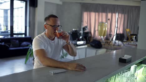 y un hombre adulto con gafas se sienta en el mostrador del bar y toma un sorbo de un cóctel de color rojo