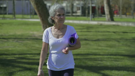 Vista-Frontal-De-Una-Mujer-Caminando-En-El-Parque,-Sosteniendo-Una-Estera-De-Yoga-En-La-Mano.