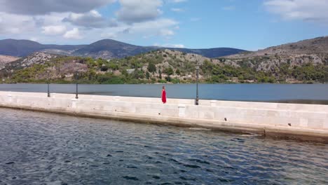 woman in red dress walking on de bosset bridge in argostoli city on kefalonia island