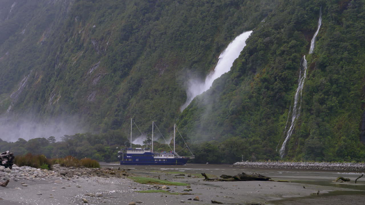 밀포드 사운드 (milford sound) 의 폭포 앞 항구에 들어오는 3 마스트 보트의 4k 영상 - 피오피오타히, 뉴질랜드