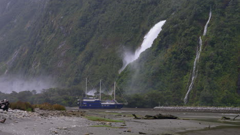 4K-footage-of-three-masted-boat-entering-the-harbour-in-front-of-a-waterfall-in-Milford-Sound---Piopiotahi,-New-Zealand