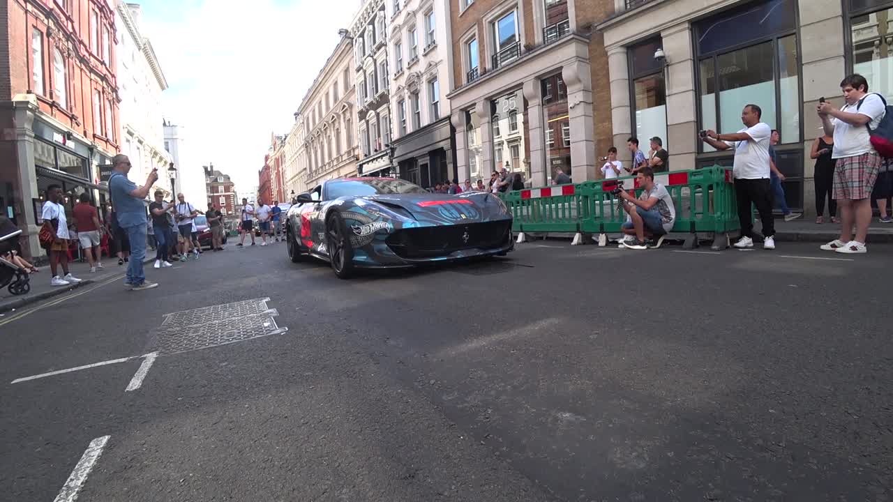 Low angle track shot of dope ferrari driving on the roads of London. People taking photos of the cars.