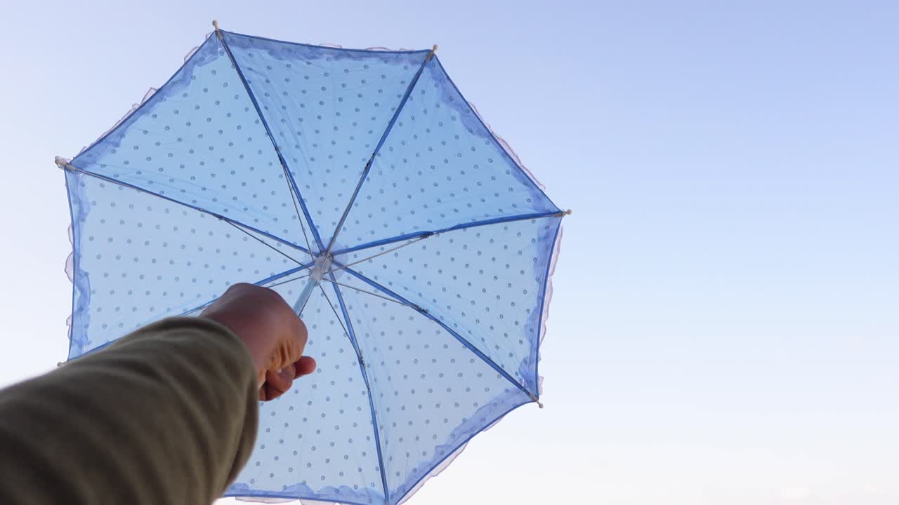 Woman Holding a Blue Dotted Umbrella Against a Blue Sky