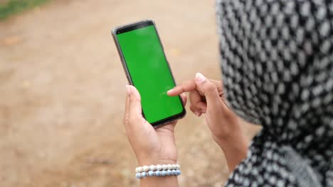a woman wearing a hijab touches the screen of a green screen phone