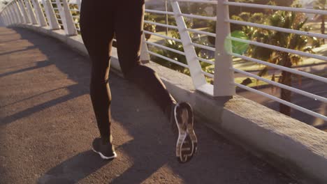 rear view of fit african american man exercising outdoors in city, running on footbridge