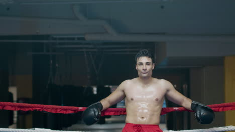 athletic man leaning on boxing ring ropes