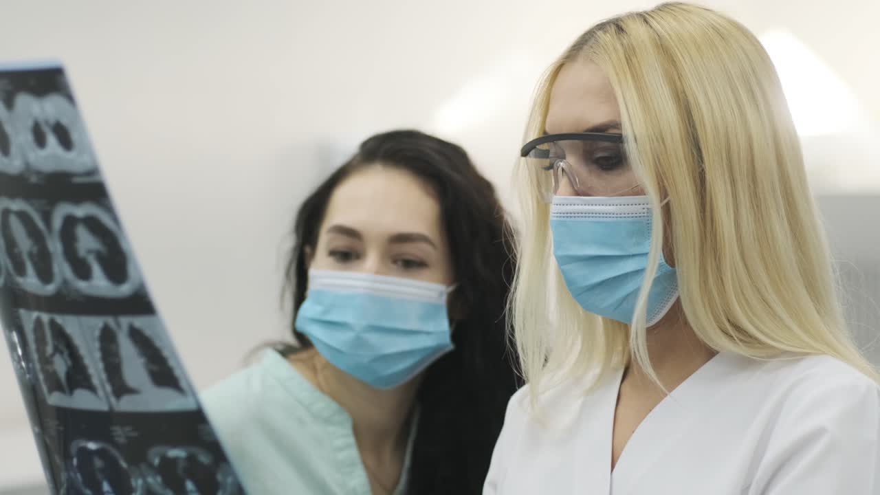 Woman doctor radiologist explains the results of CT scanning for young female patient, showing the snapshot with images, observing and analyzing CT scan in modern clinic beside modern CT scanner