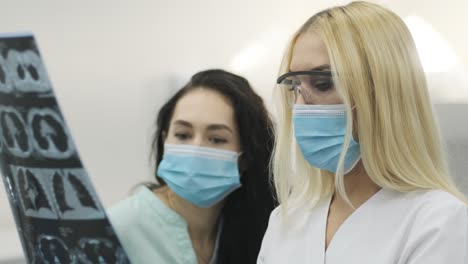 woman doctor radiologist explains the results of ct scanning for young female patient, showing the snapshot with images, observing and analyzing ct scan in modern clinic beside modern ct scanner