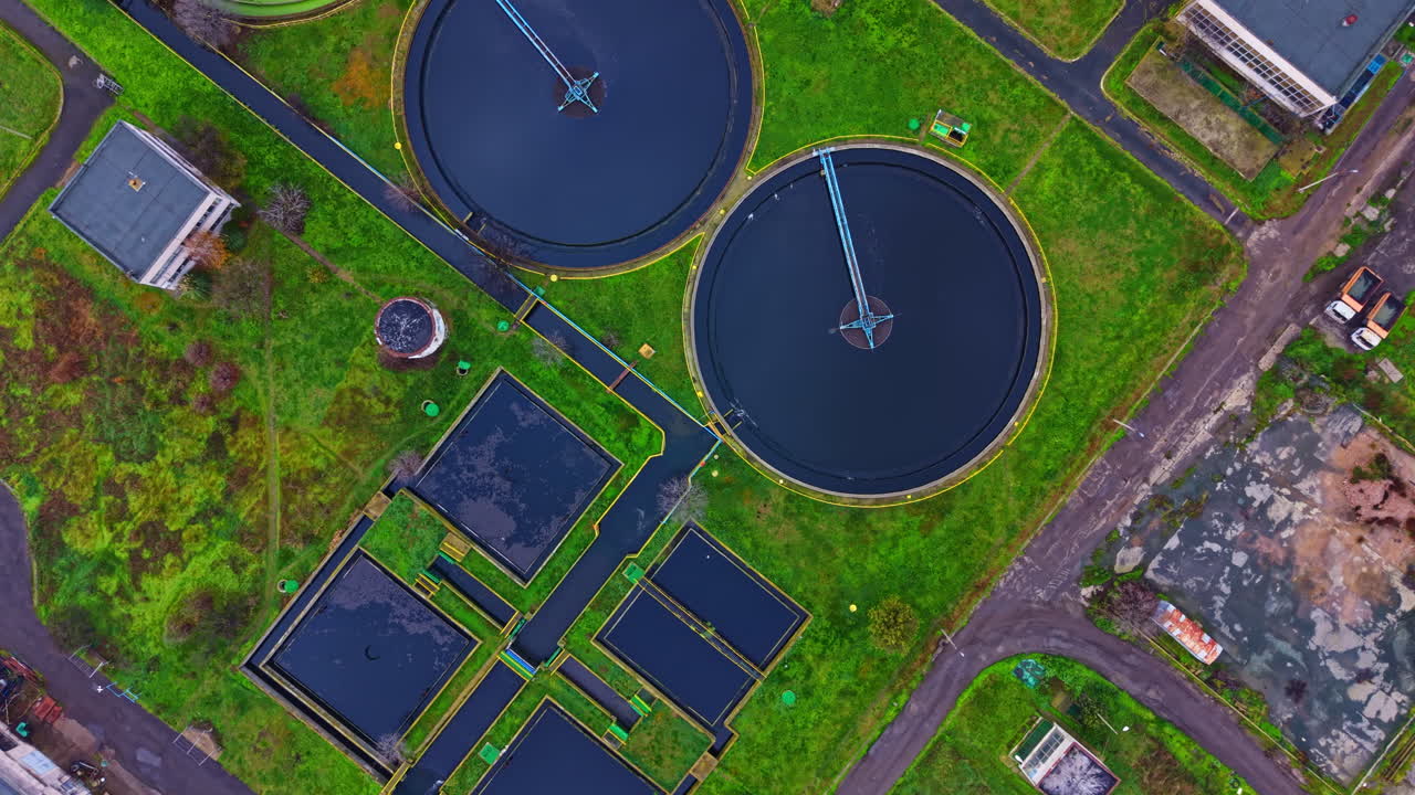View of a wastewater treatment plant from above showing multiple water treatment tanks and greenery around the area during daytime
