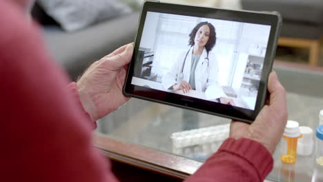 hombre caucásico anciano usando tableta para consulta en línea con una doctora biracial, cámara lenta