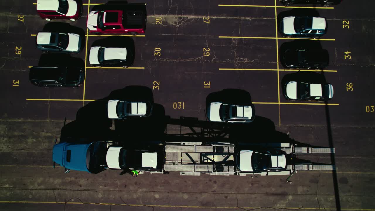 Overview Top down of truck driver on top of deck of a stinger carhauler securing new loaded cars.