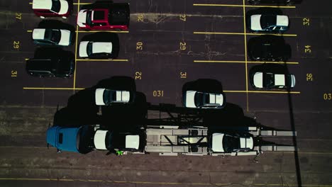overview top down of truck driver on top of deck of a stinger carhauler securing new loaded cars.