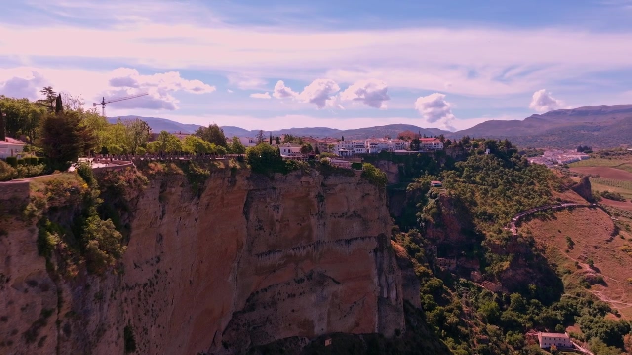 Imágenes de dron avanzando lentamente a través de un teleobjetivo, utilizando una ventana de roca natural tallada en el acantilado de Ronda como marco antes de que el campo se extienda ampliamente más allá.
