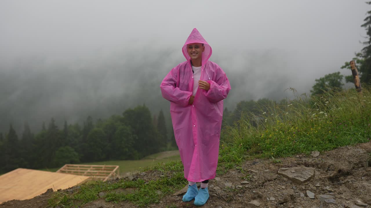 mujer con un impermeable rosa caminando en montañas de niebla