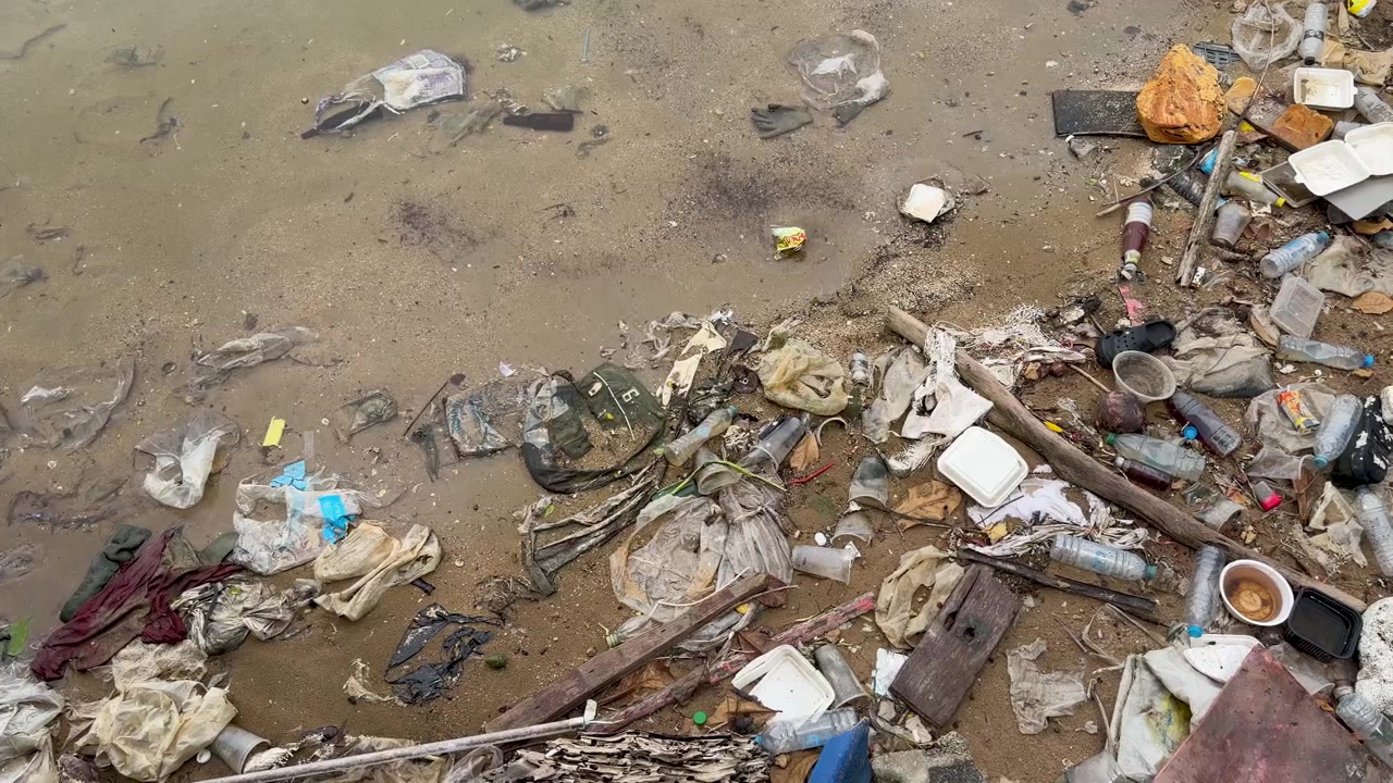 Overhead view of discarded plastic trash, styrofoam containers, and garbage polluting a muddy coastline.