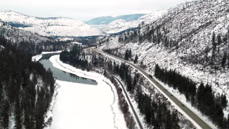 Columbia-Británica-Nevada:-Una-Perspectiva-De-Seguimiento-De-Camiones-Y-Automóviles-En-La-Autopista-5-De-Cabeza-Amarilla-Al-Lado-Del-Río-North-Thompson-Parcialmente-Cubierto-De-Nieve-Cerca-De-Kamloops,-Impresionante-Vista-Panorámica-Del-Paisaje-Nevado