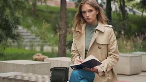 caucasian female student looking at the camera and writing in notebook.