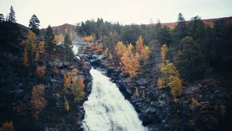 waterfall flowing in the rocky cliff with yellow trees during autumn in dovrefjell, norway