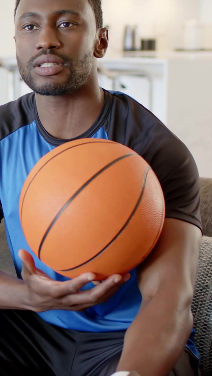 Vertical video: Looking left, speaking, reaching for pizza, man holding ball on couch in blue shirt
