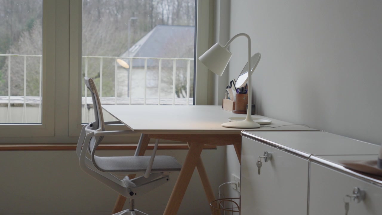 A clean and modern home office setup featuring a white desk, ergonomic chair, and bright window.