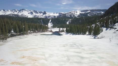 amplia toma aérea de un lago congelado ubicado en la base de picos nevados